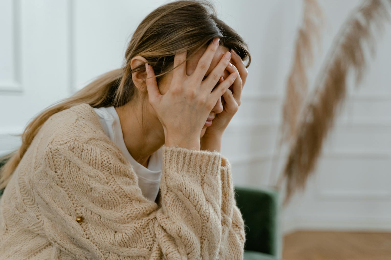 Foto: Pexels A woman sitting indoors covering her face in frustration, depicting stress and mental health challenges.