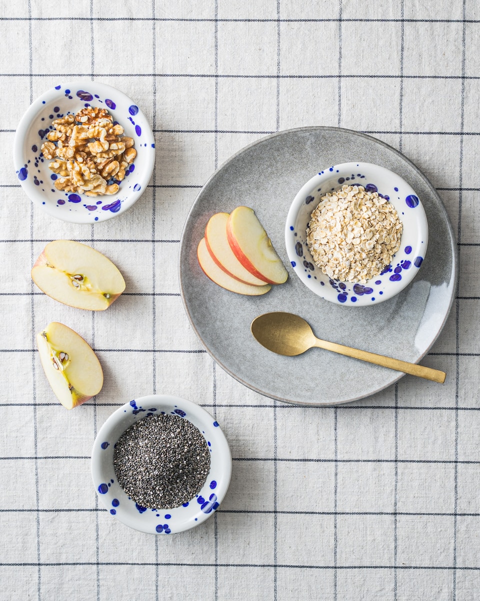 a bowl of oatmeal, apple slices, and spoon on a plate