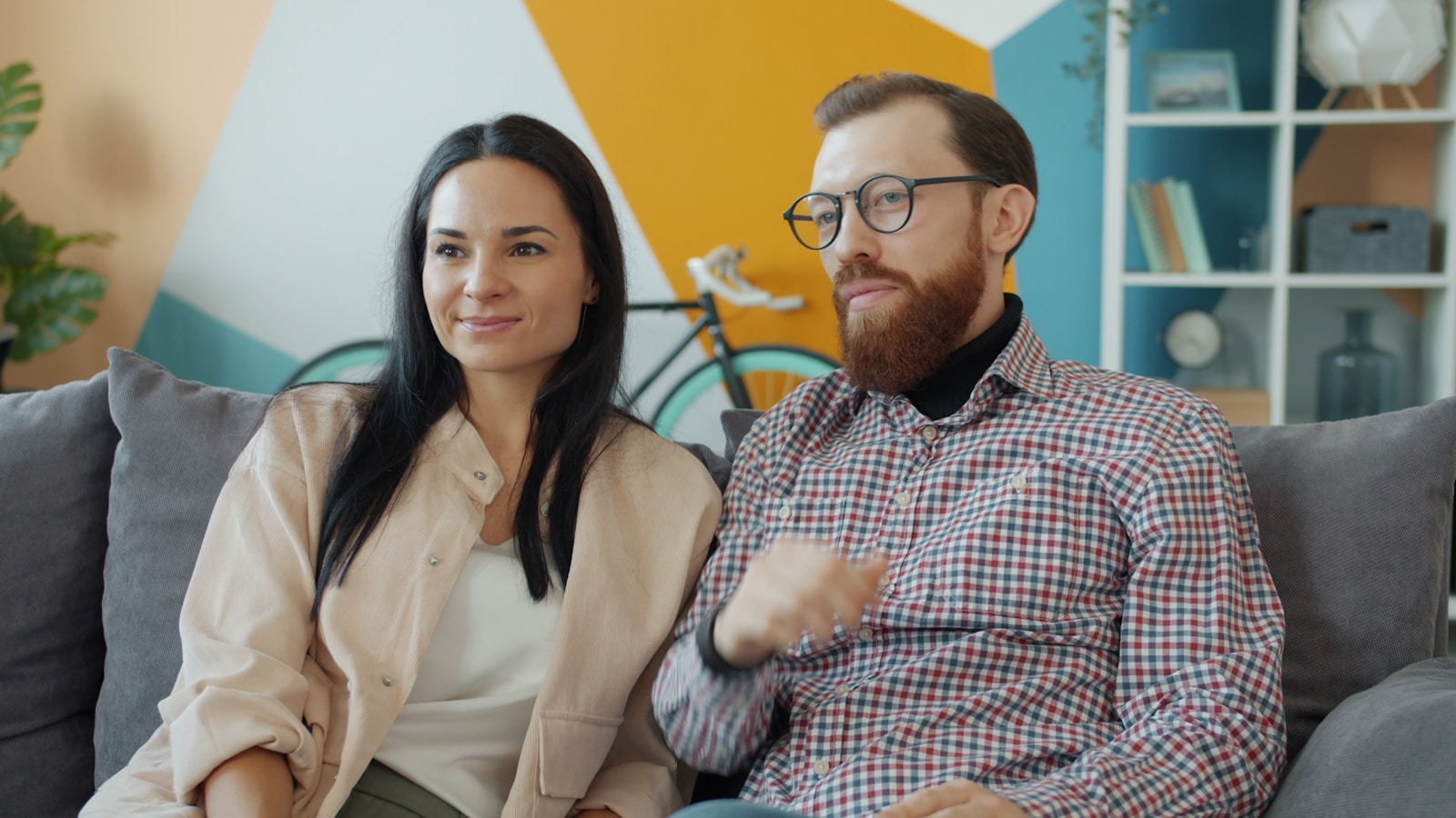 Couple sitting on a couch watching something.