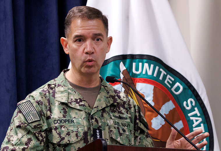 Američki admiral u uniformi Ratne mornarice, sa imenom 'COOPER' na grudima, govori ispred zastave Sjedinjenih Američkih Država i pečata Ratne mornarice.