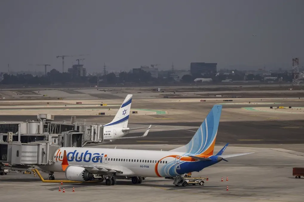 Avion kompanije Flydubai parkiran na aerodromu, povezan sa izlazom za ukrcavanje, pored aviona sa zastavom Izraela.