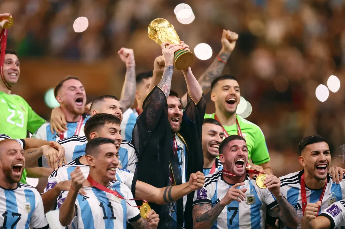 Lionel Messi drži pehar Svjetskog prvenstva iznad glave, okružen oduševljenim saigračima iz reprezentacije Argentine, nakon pobjede na FIFA Svjetskom prvenstvu 2022.
