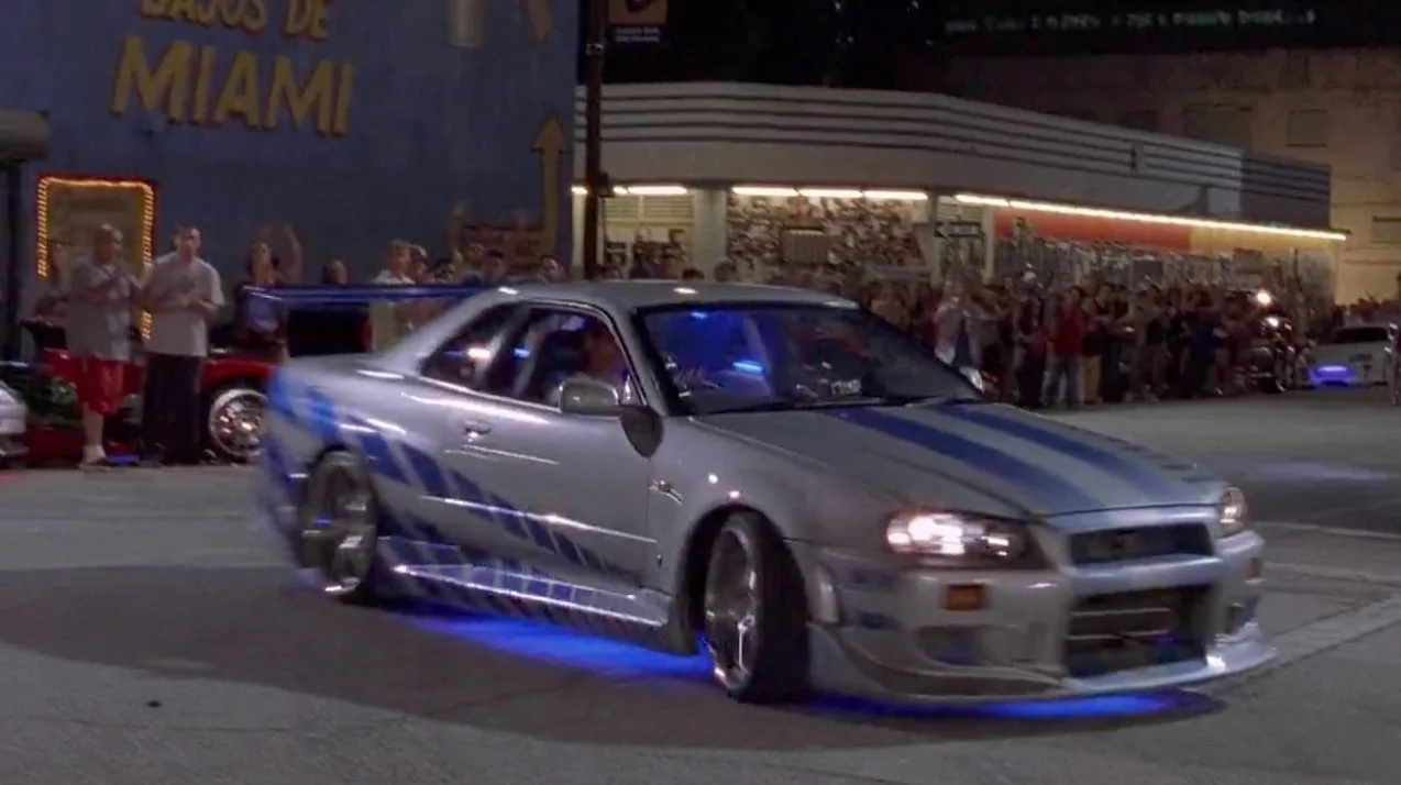 Srebrni sportski automobil sa plavim prugama i neonskim osvjetljenjem vozi se ulicom