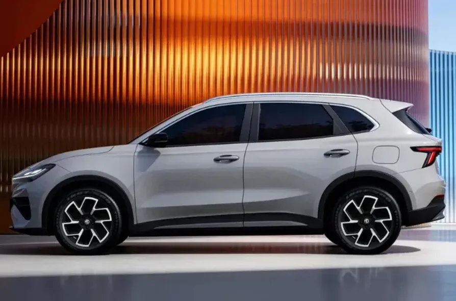 Sivi SUV automobil iz profila s tamnim staklima i modernim naplatcima, postavljen ispred pozadine s vertikalnim rebrastim elementima u narančastoj i plavoj boji.