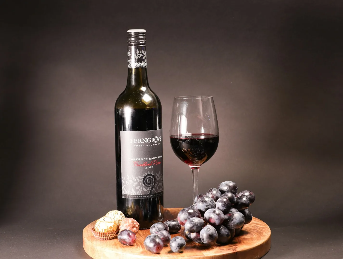 Boca crnog vina Cabernet Sauvignon uz čašu istog vina i grozd tamnog grožđa.