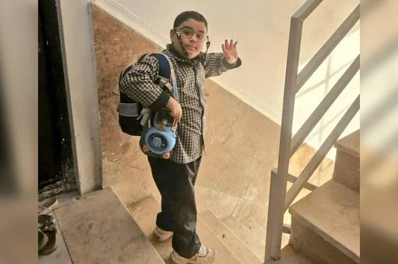 Dječak sa rancom na leđima i plavom loptom u ruci maše na stepenicama.