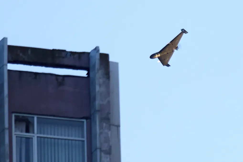 Crni dron trouglastog oblika u letu na nebu, pored zgrade.