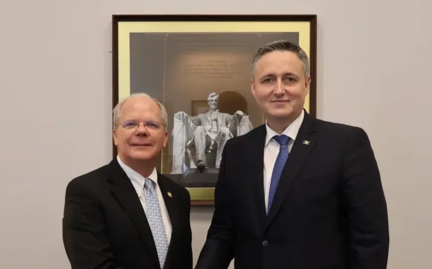 Dva muškarca u tamnim odijelima stoje ispred slike Abrahama Linkolna.