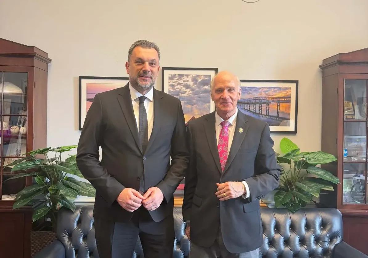 Dva muškarca u odijelima poziraju u uredskom okruženju.