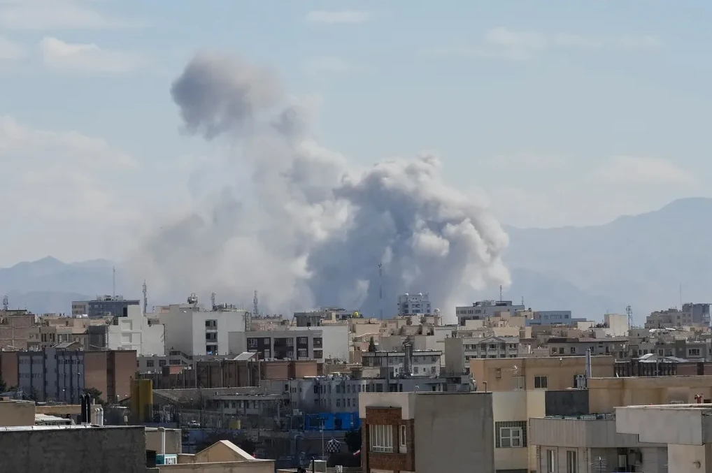 Veliki oblak dima nadvija se nad urbanim pejzažem s planinama u pozadini.