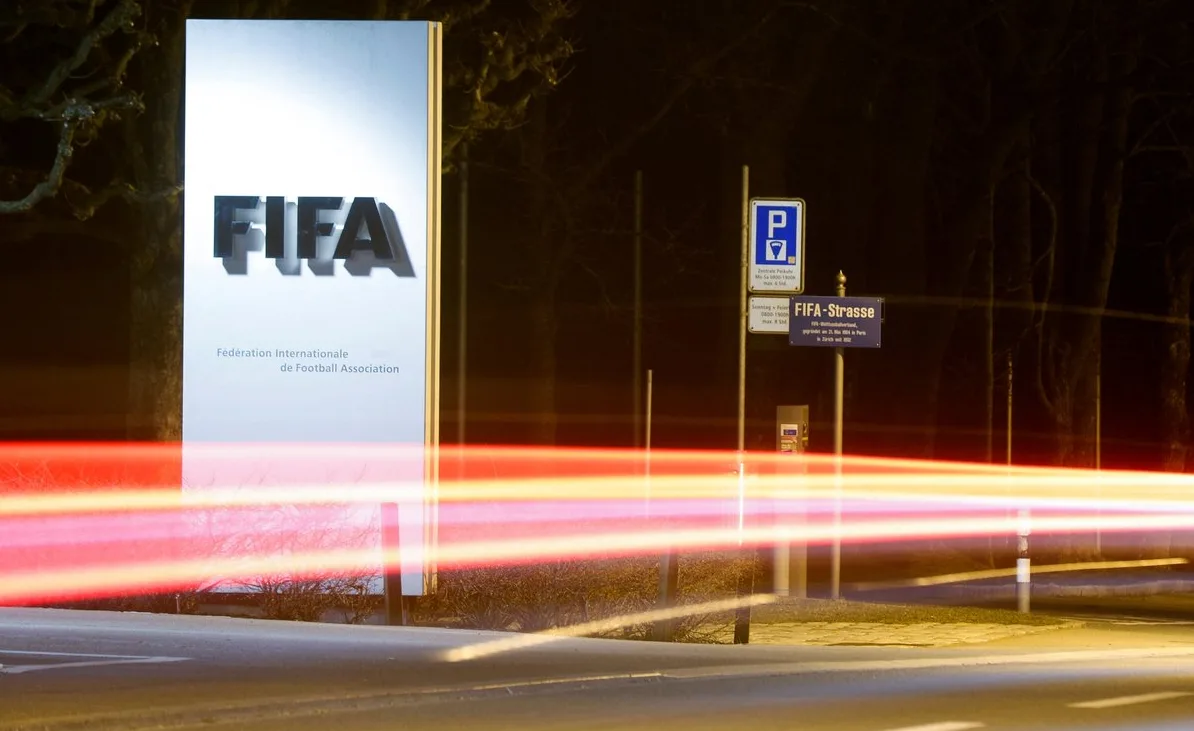 FIFA-in znak s natpisom na francuskom i njemačkom jeziku, zajedno s drugim znakovima i svjetlosnim tragovima automobila ispred sjedišta FIFA-e noću.