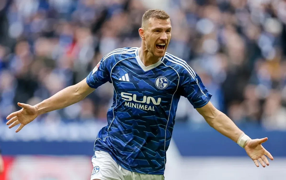 Fudbaler u plavom dresu FK Šalke 04 sa raširenim rukama i uzvikom.