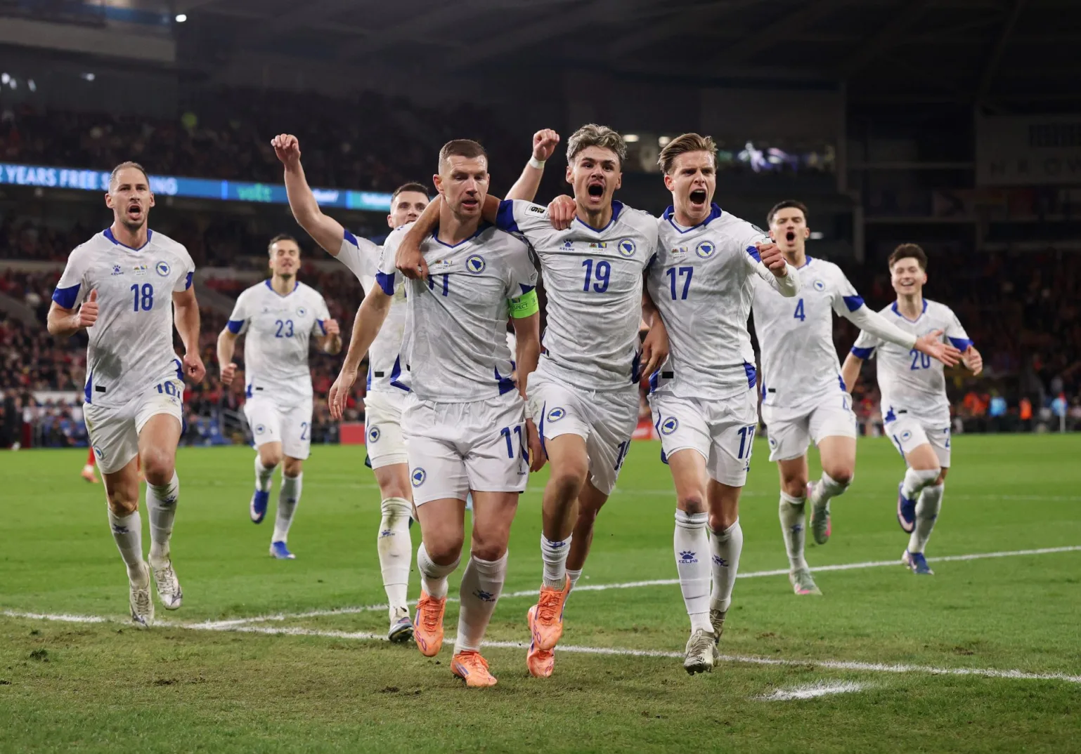 Fudbaleri Bosne i Hercegovine u bijelim dresovima slave pogodak na zelenom terenu stadiona.