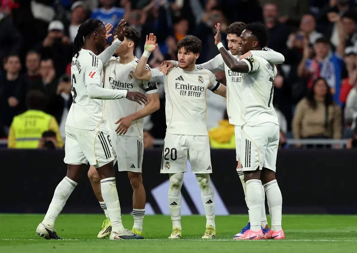 Grupa fudbalera Real Madrida u bijelim dresovima slave gol na zelenom travnjaku stadiona.