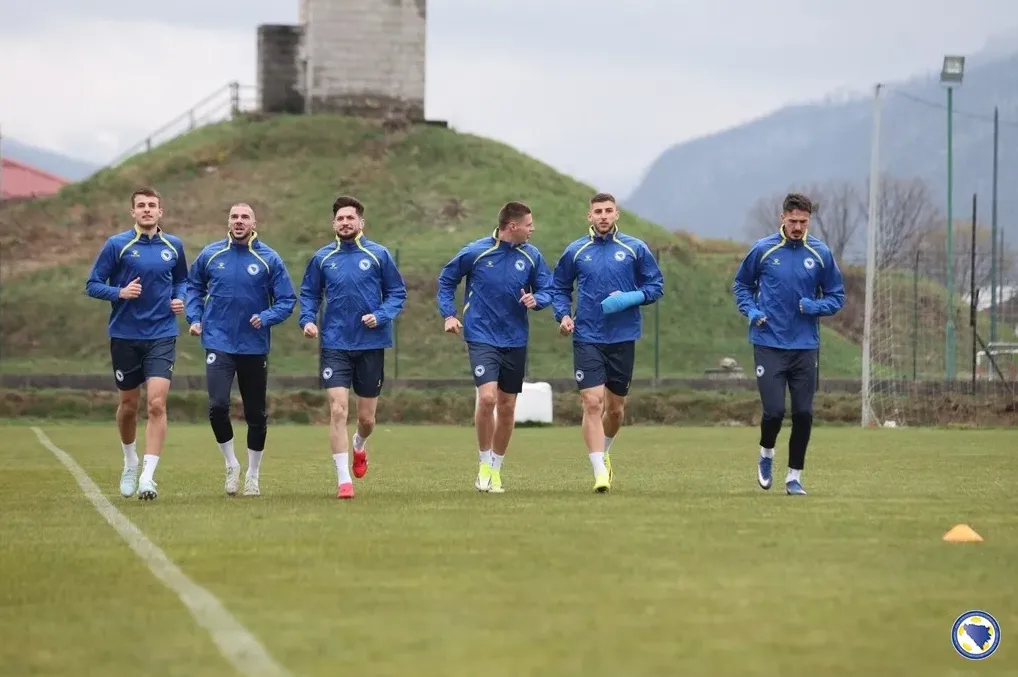 Fudbaleri u plavim dresovima trče na zelenom terenu.