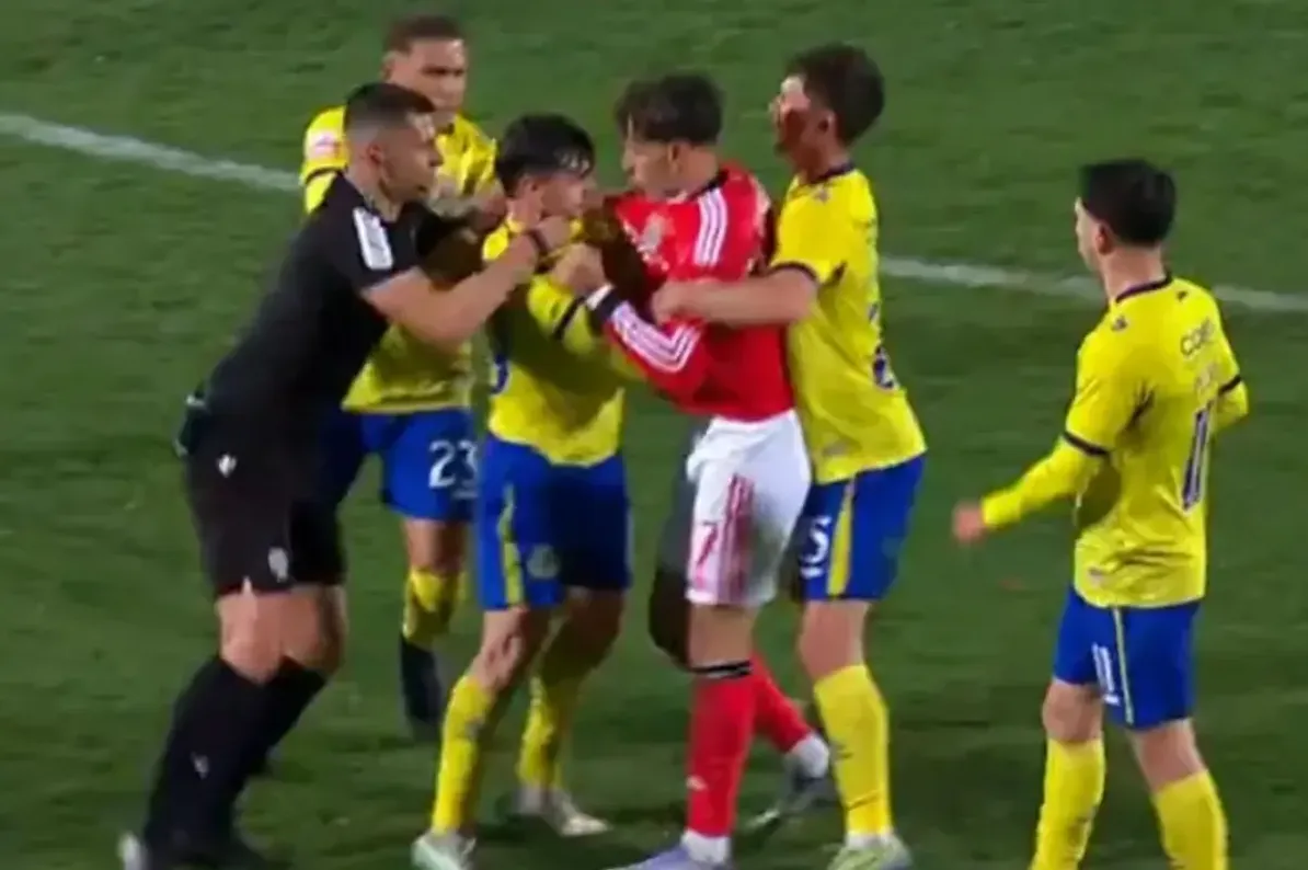 Fudbaler u crvenom dresu se rve sa igračem u žutom dresu, dok im sudija i drugi igrači pokušavaju razdvojiti.