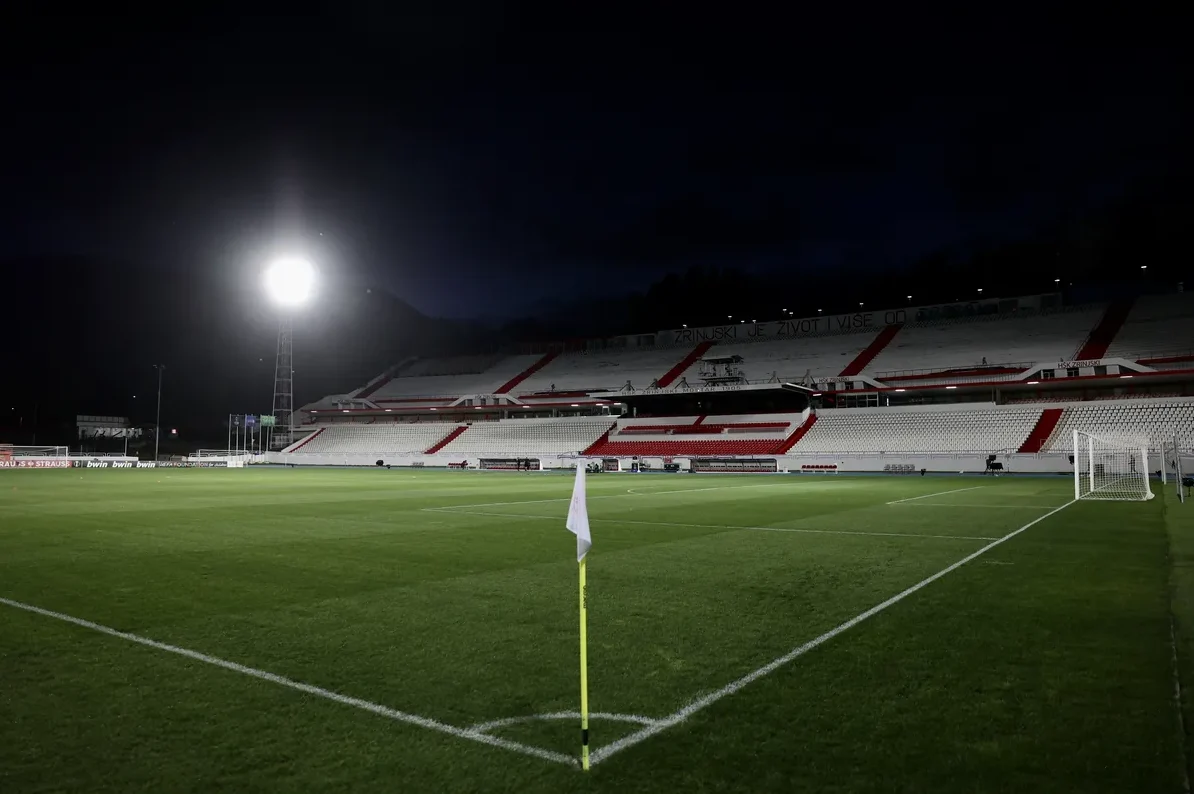 Fudbalski stadion "Pod Bijelim Brijegom" u Mostaru noću, osvijetljen reflektorima, sa praznim tribinama i zelenim terenom.