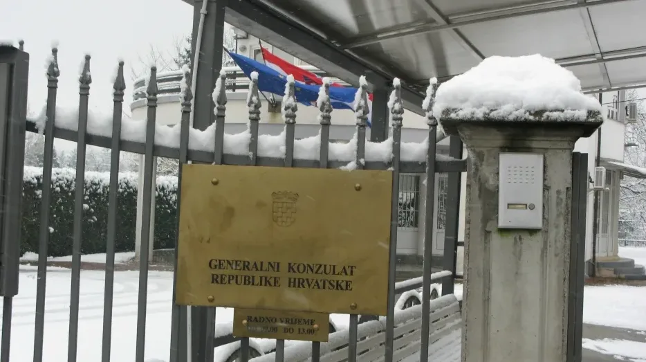Generalni konzulat Republike Hrvatske s natpisnom pločom i zastavama, prekriven snijegom.