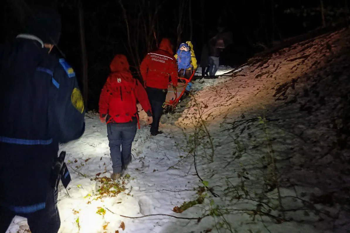 Gorska služba spasavanja nosi nosila sa povrijeđenom osobom kroz šumu prekrivenu snijegom tokom noći.