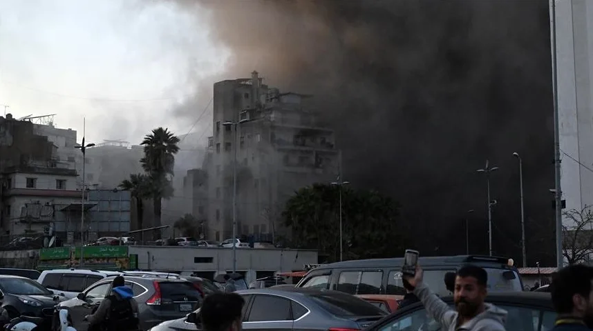 Gusta crna dimna zavjesa kulja iz zgrade u plamenu, dok su automobili parkirani u haosu ispred, a ljudi posmatraju scenu.