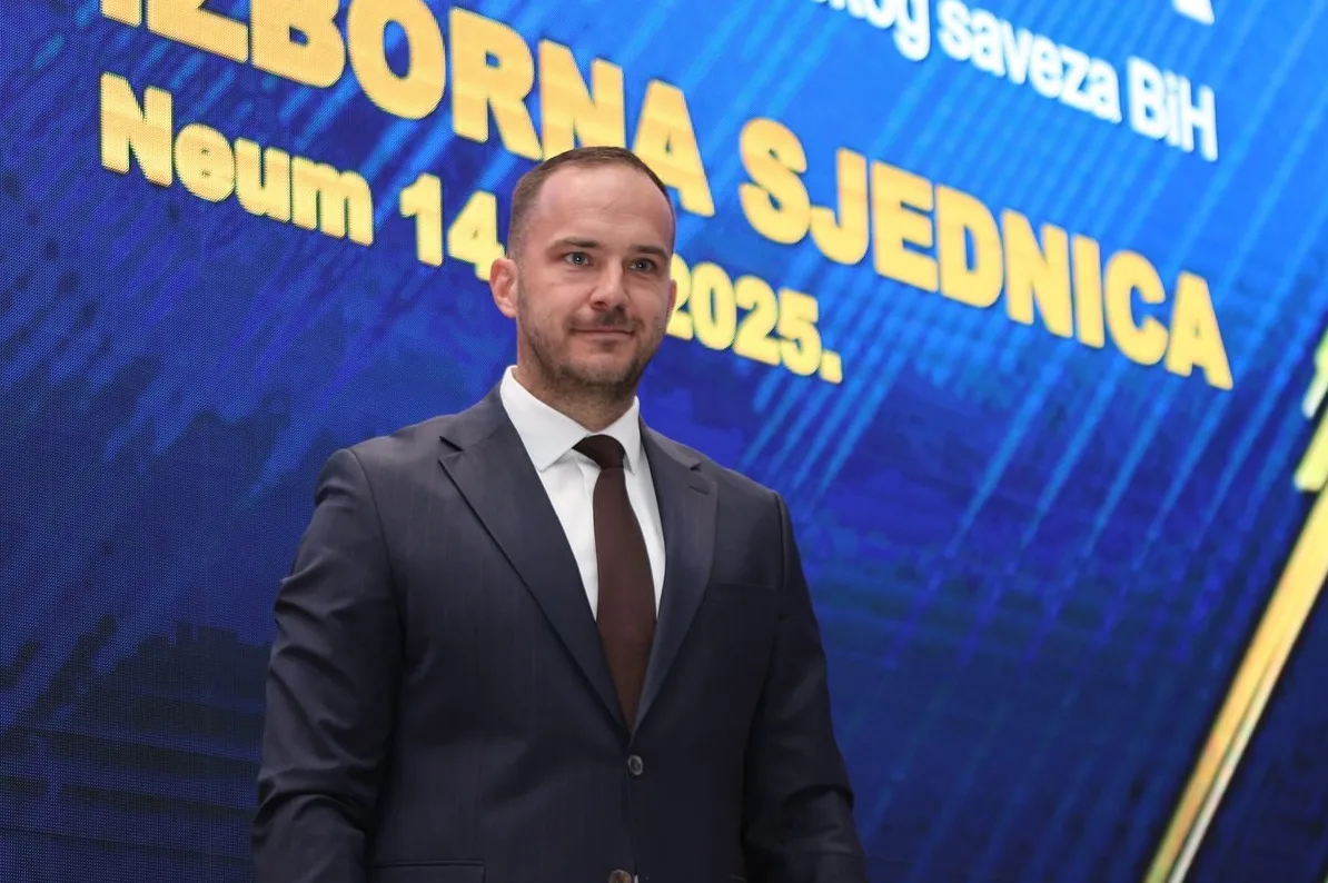 Političar u tamnom odijelu i smeđoj kravati, sa natpisom "IZBORNA SJEDNICA" i "Neum 14. 2025." u pozadini.