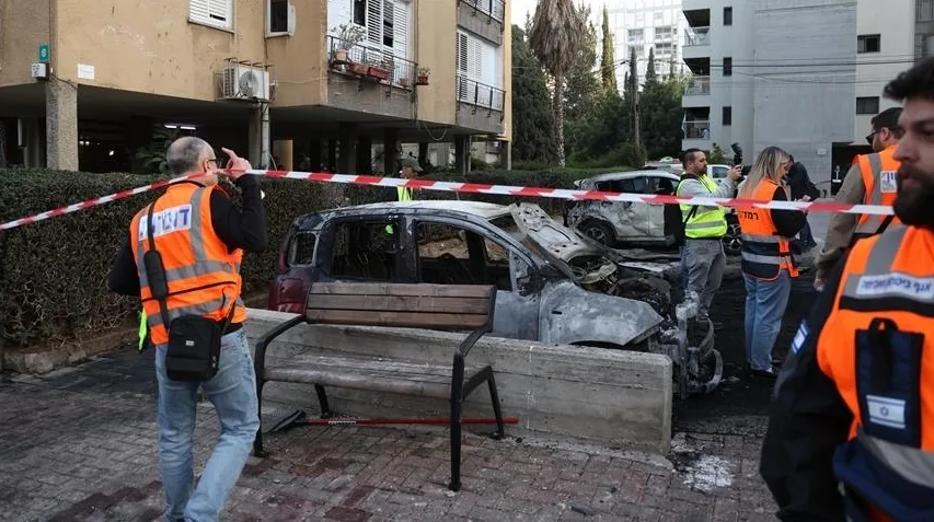 Potpuno izgorjeli automobil, okružen trakom za obilježavanje, sa istraznim radnicima u narandžastim prslucima koji pregledavaju mjesto događaja.