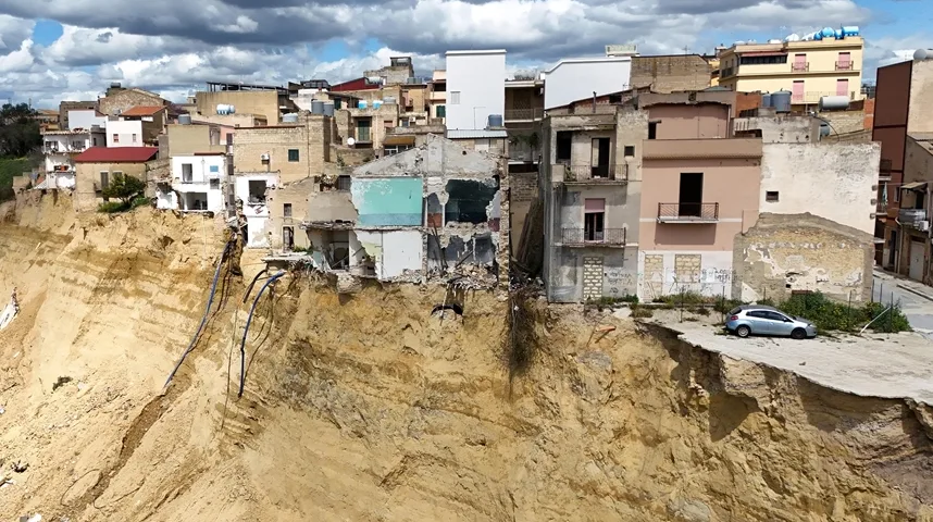 Oštećene zgrade na ivici klizišta terena sa izloženim temeljima.