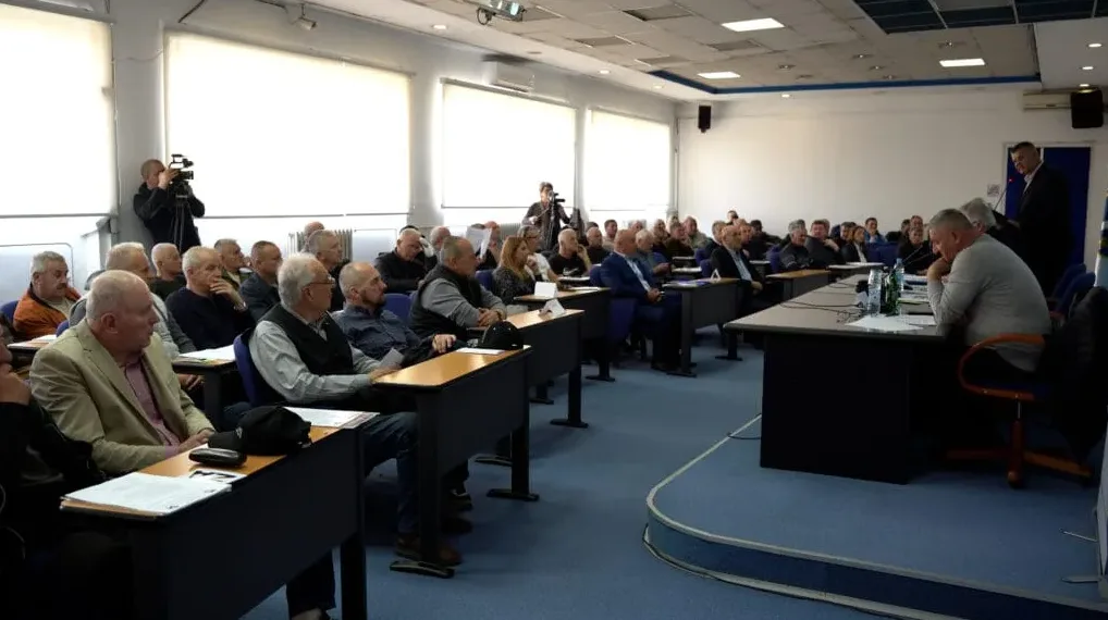 Grupa ljudi sjedi u učionici, sluša predavanje, a jedan čovjek stoji za govornicom.