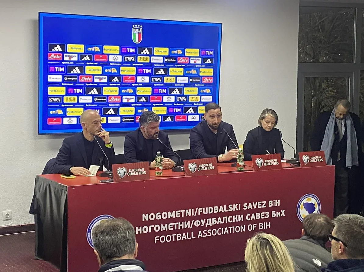 Na slici je prikazana konferencija za medije na kojoj sjede predstavnici Nogometnog/Fudbalskog saveza BiH i nogometne reprezentacije Italije. U pozadini se vidi veliki ekran sa logom Italije i logotipima sponzora, te natpisima "European Qualifiers". Ispred govornika se nalazi crveni stolnjak sa natpisom "NOGOMETNI/FUDBALSKI SAVEZ BIH FOOTBALL ASSOCIATION OF BIH".