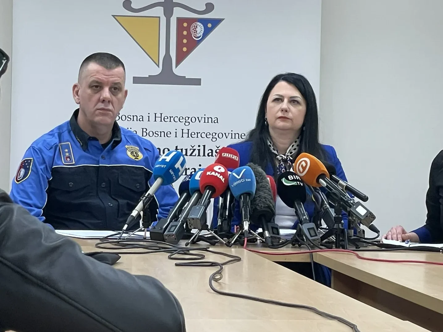 Dvoje zvaničnika sjede za stolom pred mnoštvom mikrofona na konferenciji za medije.