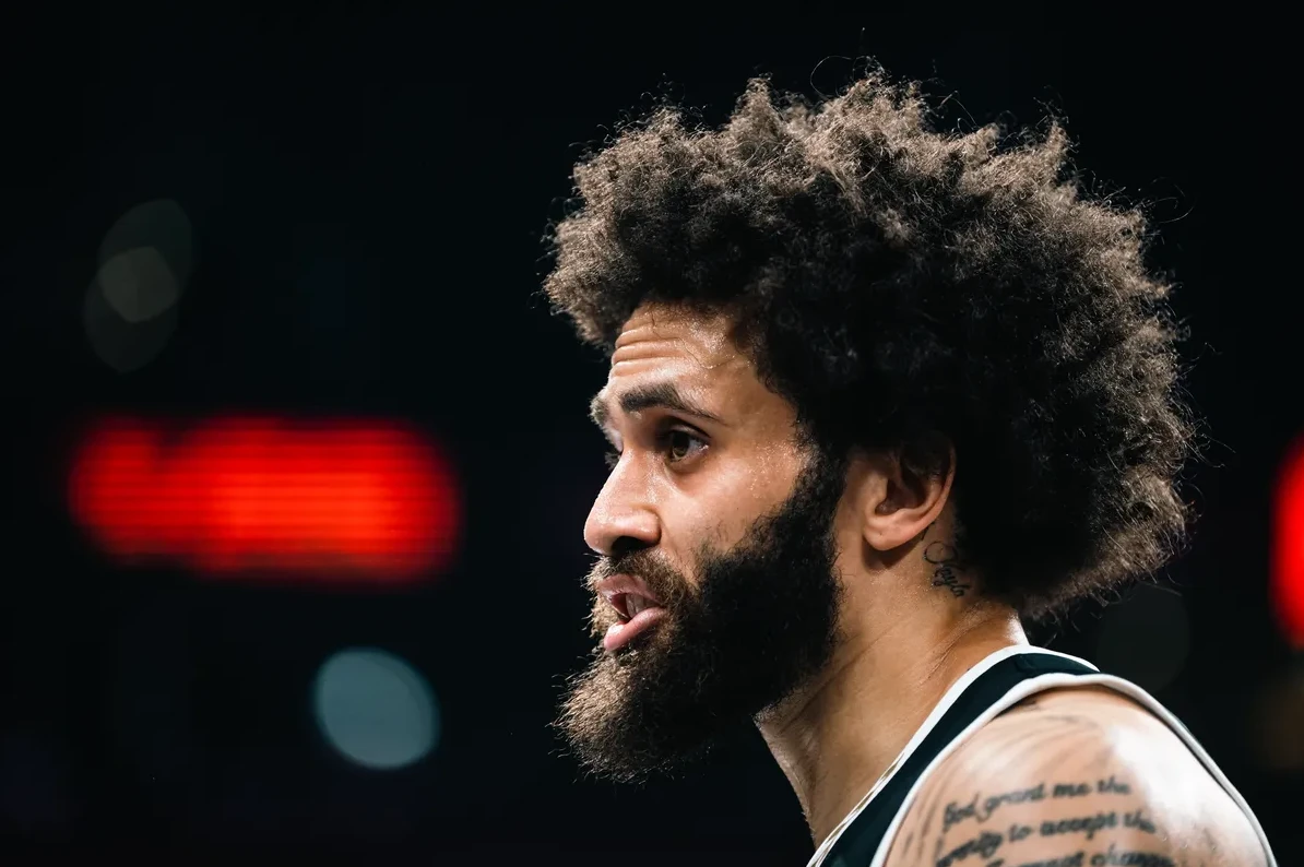 Portret košarkaša sa afro frizurom, bradom i tetovažama na vratu i ramenu.