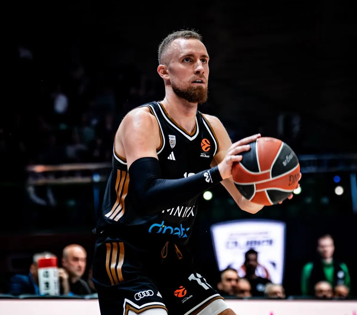 Košarkaš u crnom dresu sa zlatnim detaljima drži košarkašku loptu spreman za šut.