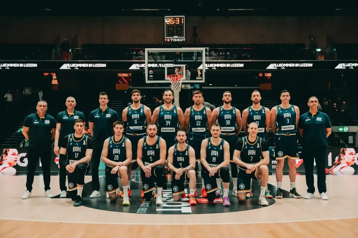 Košarkaška reprezentacija Bosne i Hercegovine pozira za timsku fotografiju u dvorani, odjevena u tamnoplave dresove sa natpisom 'BIH'.