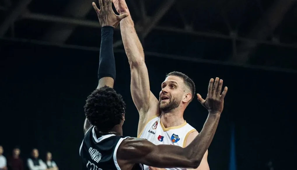 Košarkaš u bijelom dresu pokušava blokirati šut igrača u crnom dresu.