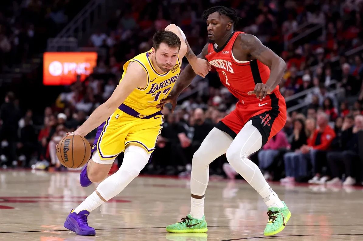 Košarkaš Los Anđeles Lejkersa u žutom dresu sa brojem 17, s loptom u rukama, u driblingu, suočen sa igračem Hjuston Roketsa u crvenom dresu sa brojem 2.