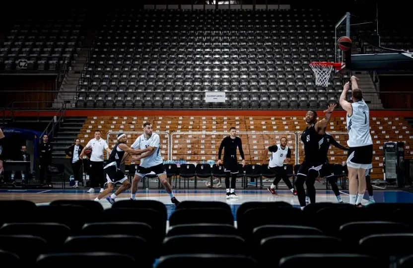 Košarkaši u crno-bijelim dresovima igraju utakmicu u praznoj dvorani.
