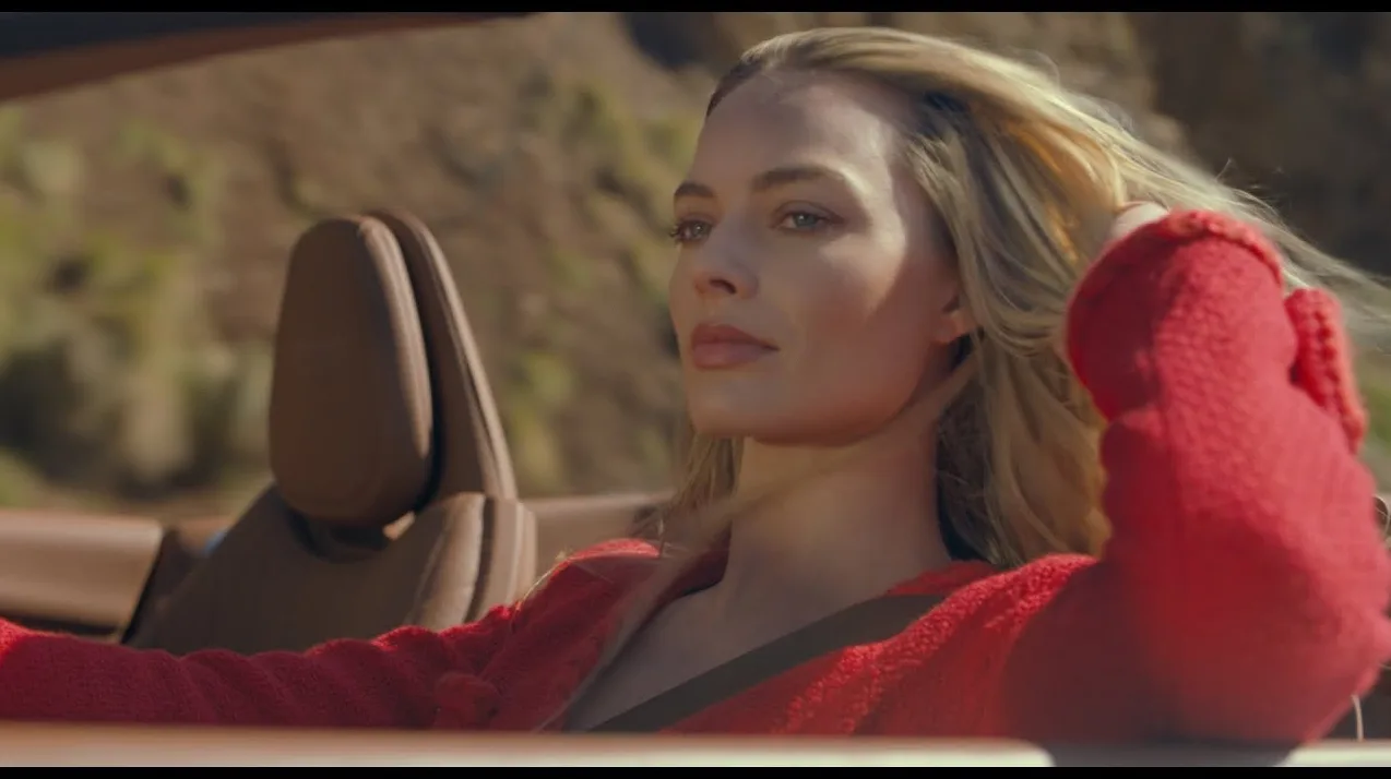 Margot Robbie nosi crveni džemper dok sjedi u kabrioletu