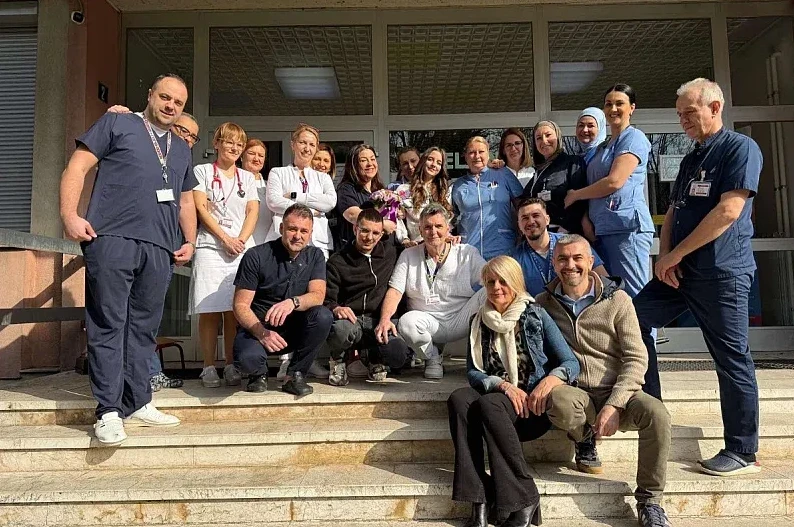 Grupa medicinskog osoblja i drugih saradnika pozira za fotografiju ispred ulaza u bolnicu.