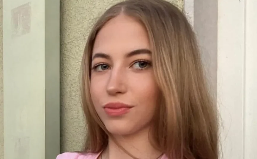 Portret mlade plavuše sa lijepim zelenim očima i blagim osmijehom, odjevene u roze majicu, slikana iznad ramena.