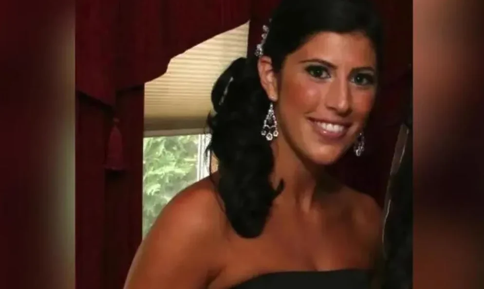 Mlada žena tamne kose i smeđih očiju, odjevena u crnu haljinu bez naramenica, sa velikim visećim naušnicama ukrašenim kristalima.