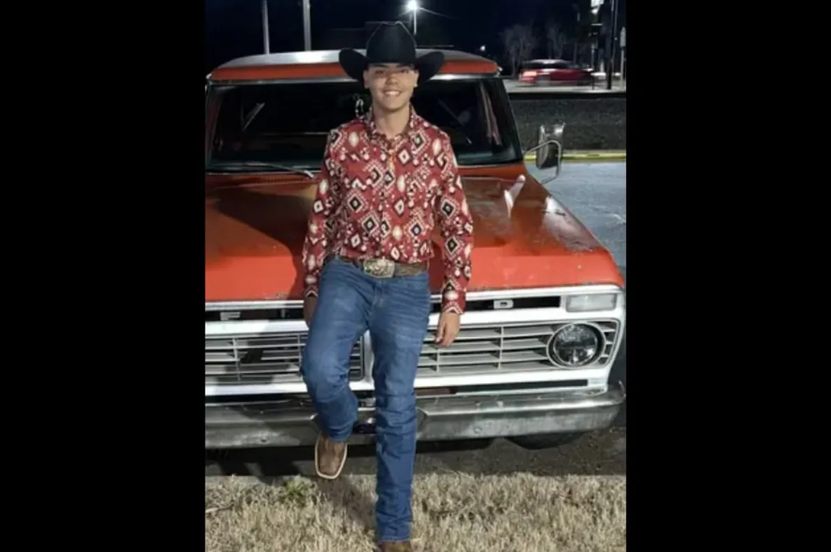 Mladić u kaubojskom šeširu i farmerkama naslonjen na stari narandžasti kamionet