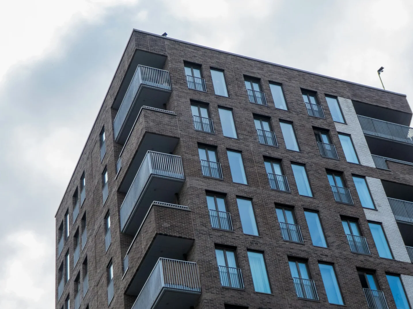 Ugao moderne stambene zgrade sa tamnim ciglama i brojnim balkonima.