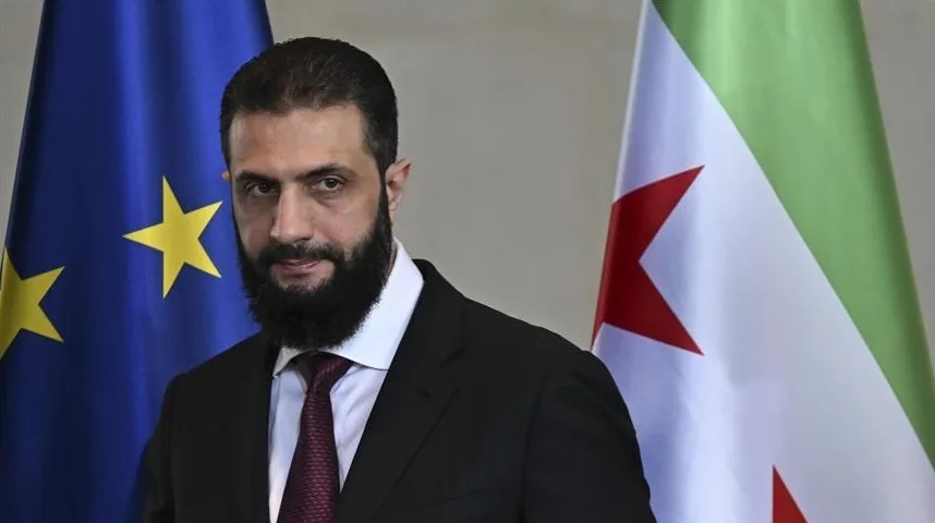 Muhamed Al Hashimi is a man with a beard, wearing a suit and tie, standing in front of the flags of the European Union and Algeria.