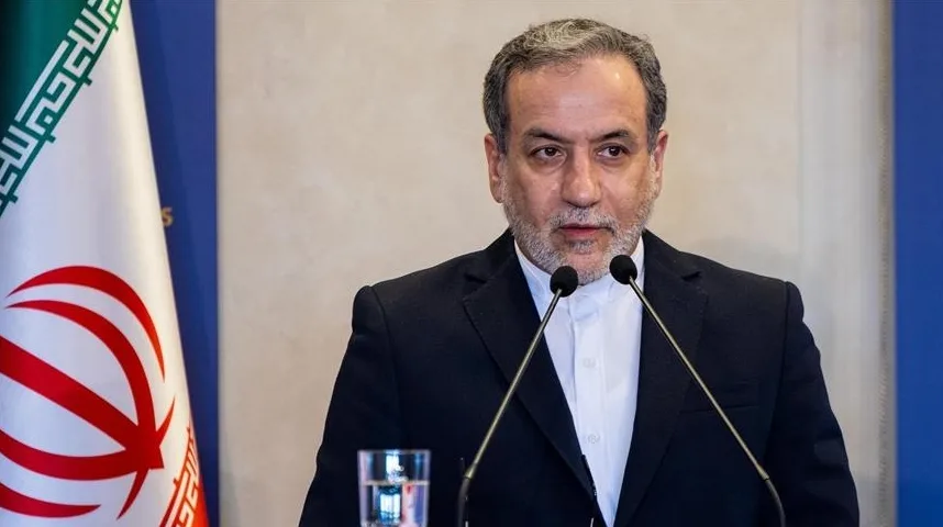 Muškarac u crnom odijelu stoji za govornicom s dva mikrofona, pored iranske zastave.