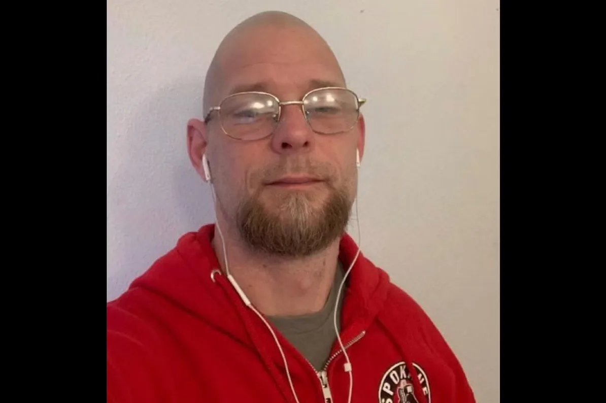 Muškarac sa obrijanom glavom, naočalama i kozjom bradicom, nosi crvenu duksericu i slušalice.