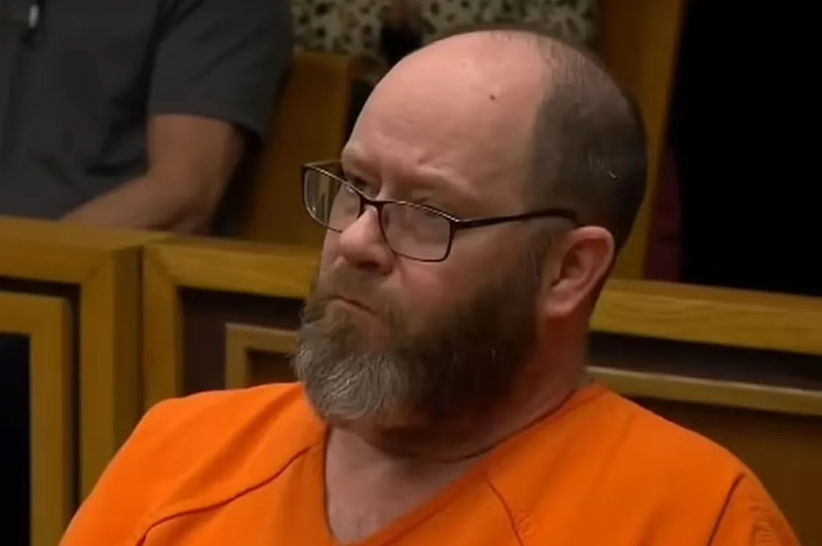 Muškarac sa naočarima i bradom u narandžastom zatvorskom odijelu gleda u stranu.