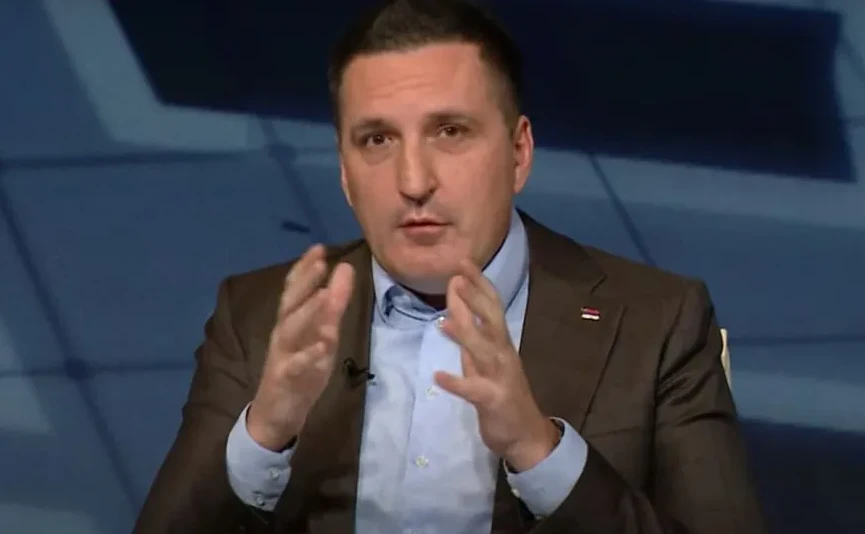 Muškarac u smeđem odijelu i plavoj košulji govori, gestikulirajući rukama.