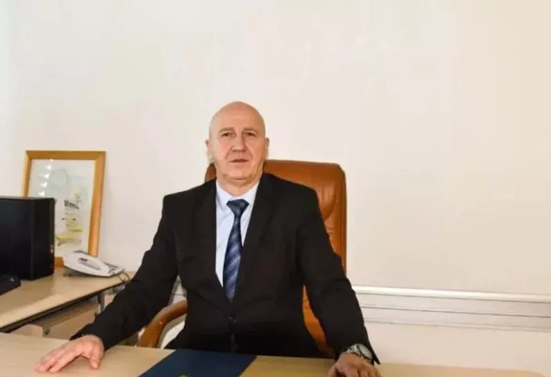 Muskarac u crnom odijelu i plavoj kravati sjedi za stolom.