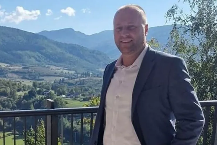 Muškarac u tamnom odijelu i bijeloj košulji nasmijan