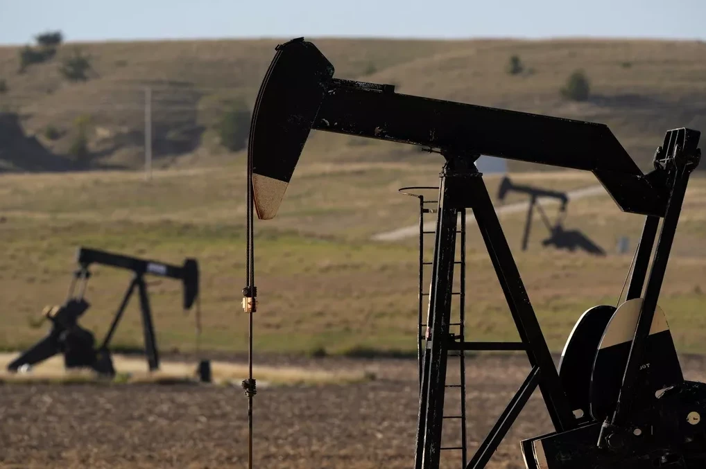 Crna naftna pumpa u prvom planu sa još nekoliko naftnih pumpi u daljini, na obradivom polju.